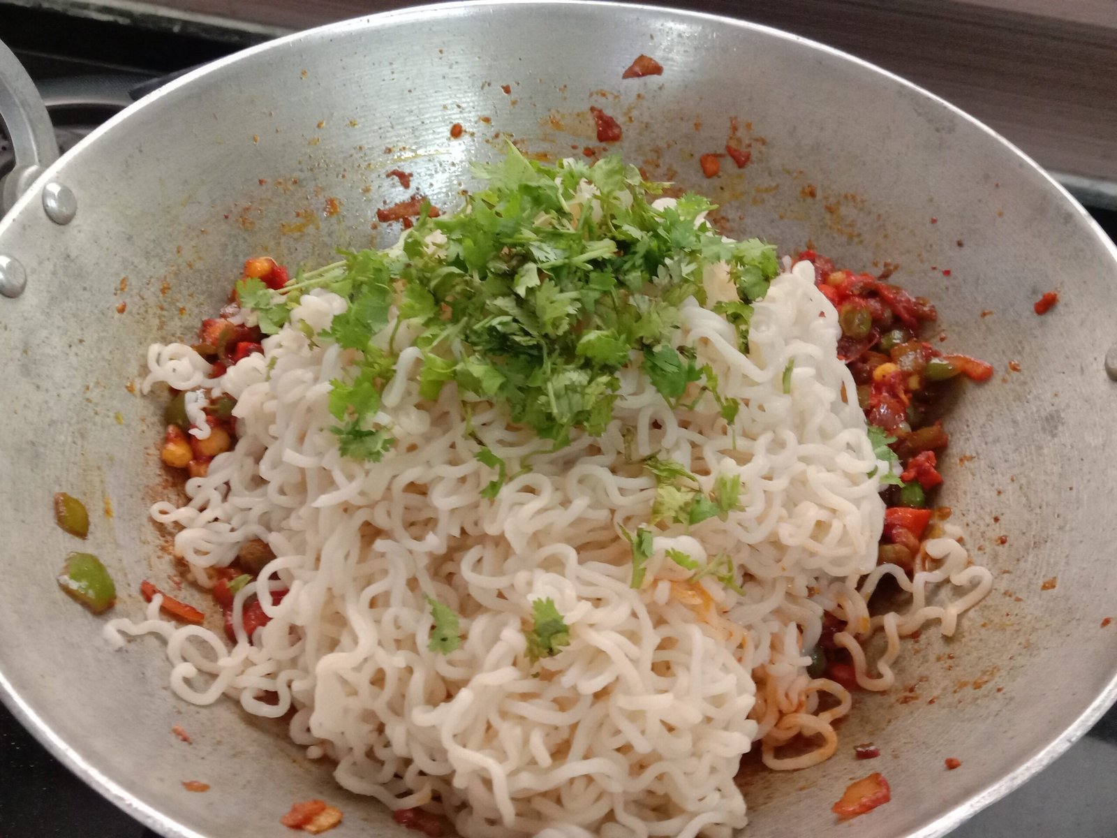 Adding coriander to ingredients, in pot, Egg bhurji maggi noodles recipe.