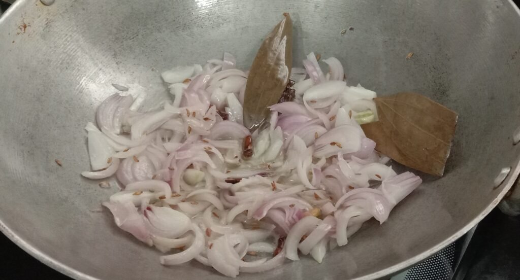 Adding sliced onion in kadhai, Chole bhature recipe.